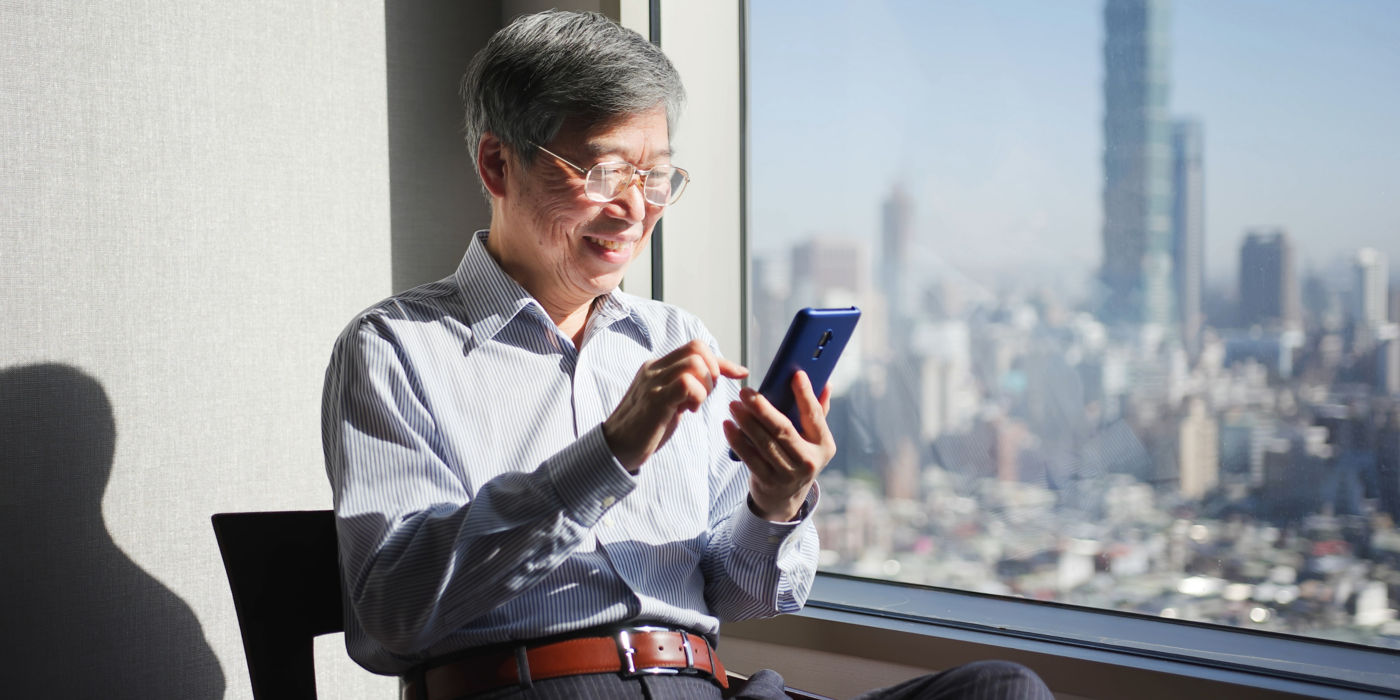 Senior Asian man using smartphone with city view from window in the background.